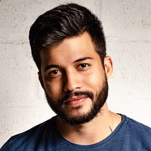 A man with dark hair and a beard, wearing a blue shirt, stands in front of a white textured wall, looking at the camera with a slight smile—a paving contractor Hunterdon serving Mercer County NJ & Bucks County PA.