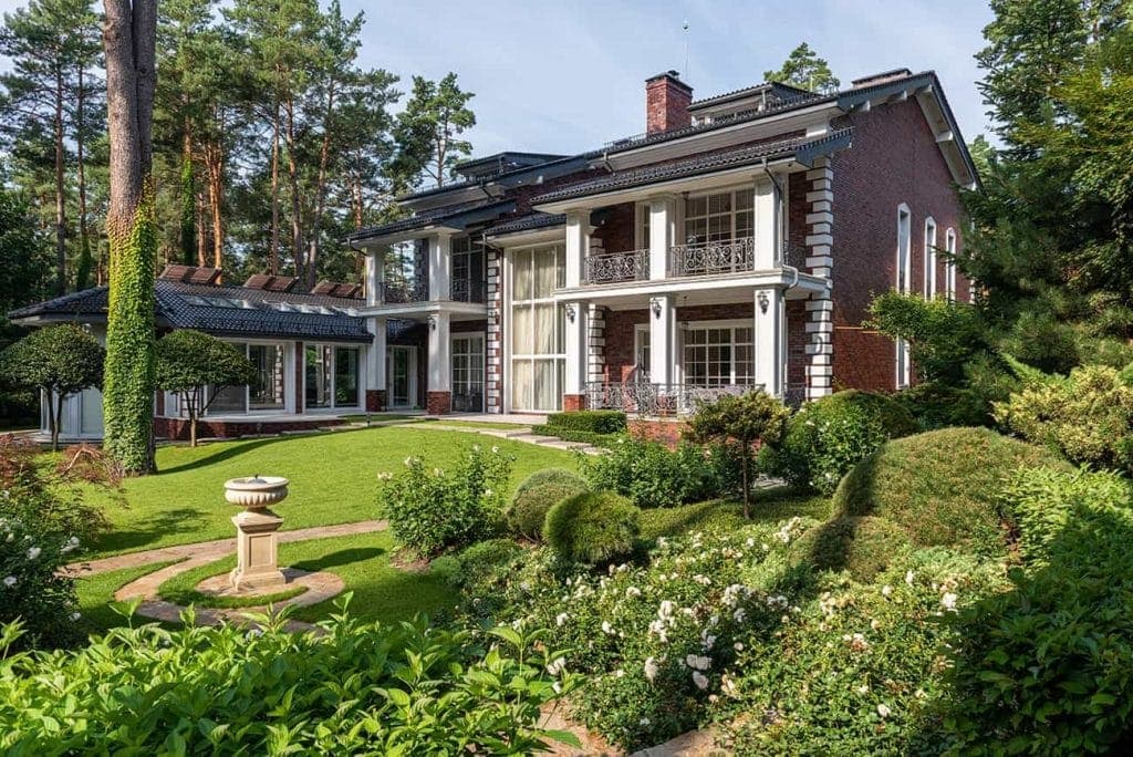 A large brick house with a lawn and trees, expertly landscaped by a paving contractor serving Hunterdon, Mercer County NJ & Bucks County PA.