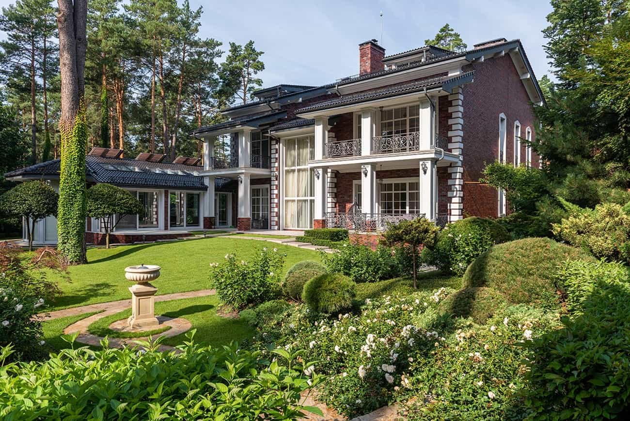 A large brick house with a lawn and trees, expertly landscaped by a paving contractor serving Hunterdon, Mercer County NJ & Bucks County PA.