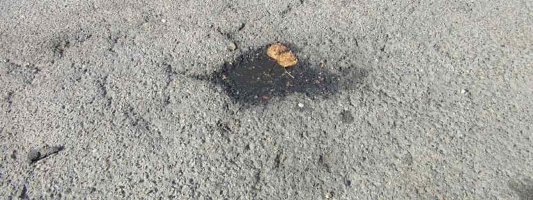 Water-filled pothole in a rough, cracked asphalt road