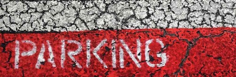 Cracked pavement with a faded white PARKING stripe