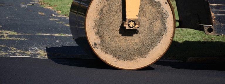 Close-up of a roller compactor smoothing fresh asphalt surface.