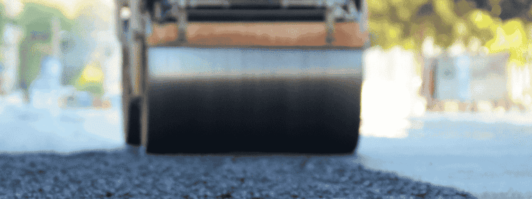 A close-up view of a road roller compacting fresh asphalt on a street in Mercer County NJ, with the roller in focus—a signature scene for any paving contractor Hunterdon trusts. The surroundings blur softly in the background.
