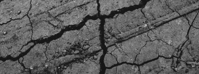Close-up view of cracked, dry asphalt pavement with deep jagged fissures running across the surface, showing rough, weathered damage. A paving contractor in Hunterdon, Mercer County, NJ & Bucks County, PA can restore areas like this.